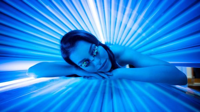a woman laying on a electric sunbed wearing goggles