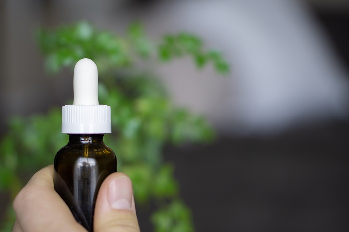 person holding a white and brown cbd oil bottle