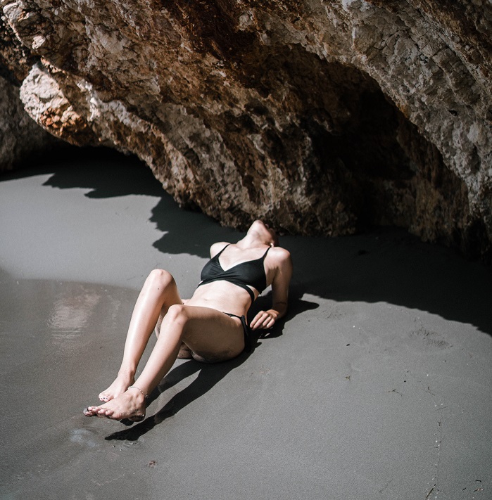 woman laying on sand near rock formation